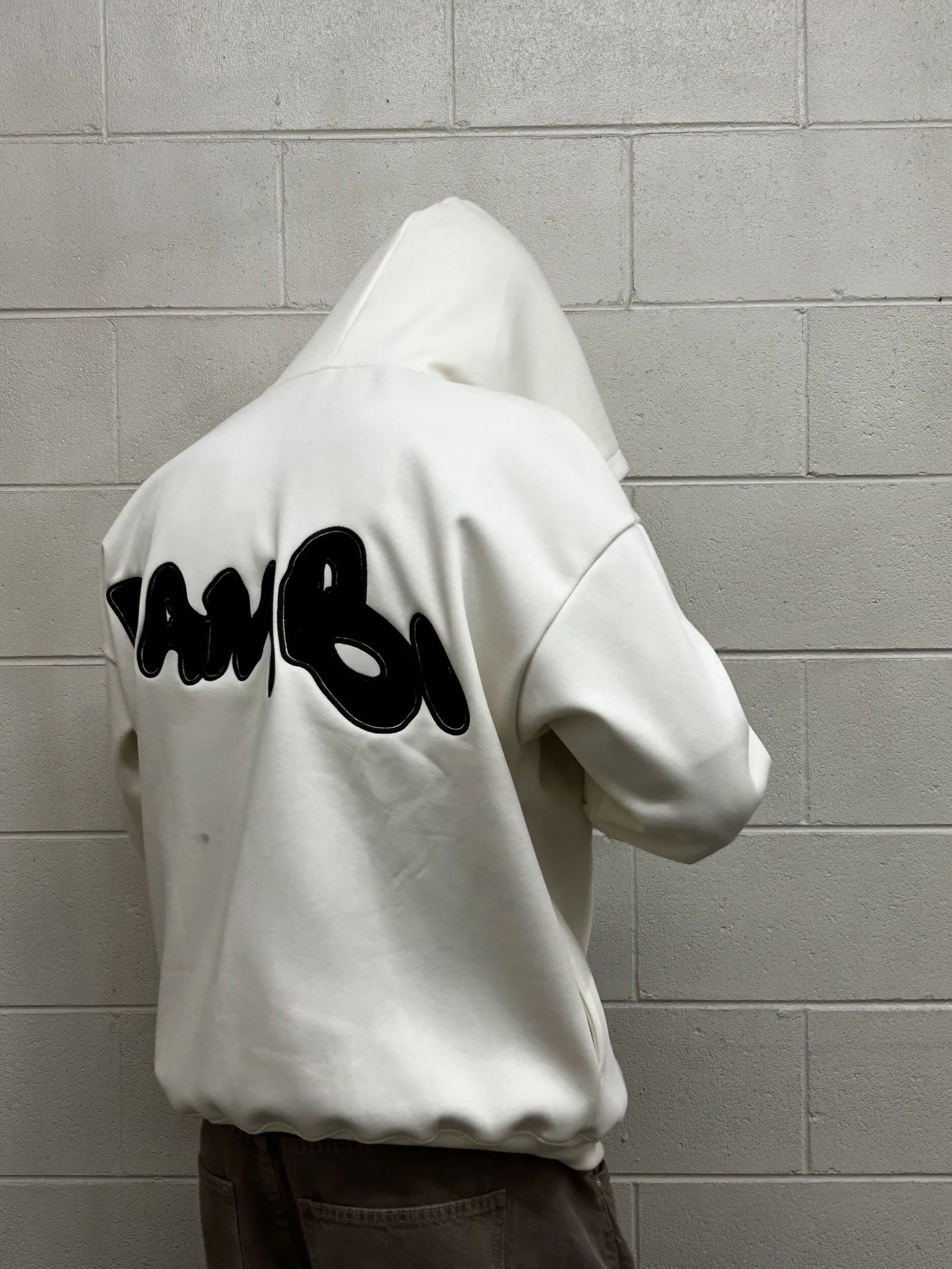 Person wearing a white hoodie with black text on the back, standing against a gray brick wall.