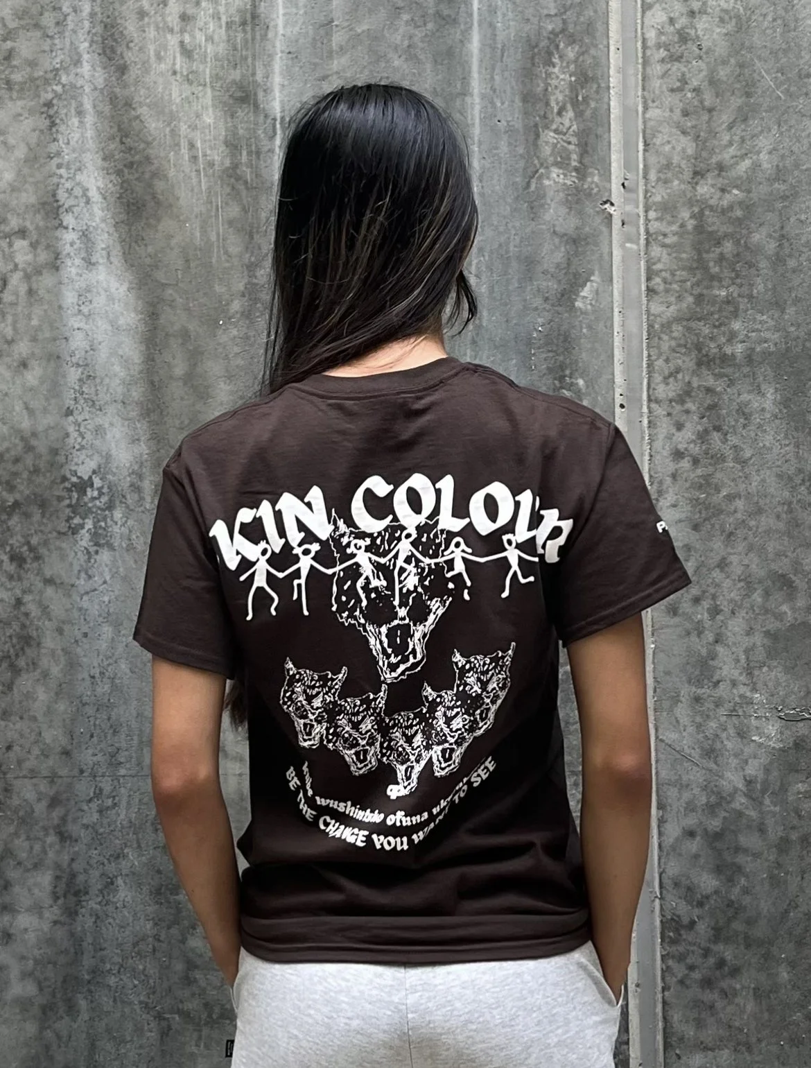 Back of a person wearing a black T-shirt with a graphic design featuring stylized wolves and the words 'KIND COLOR' and an inspirational quote about changing.