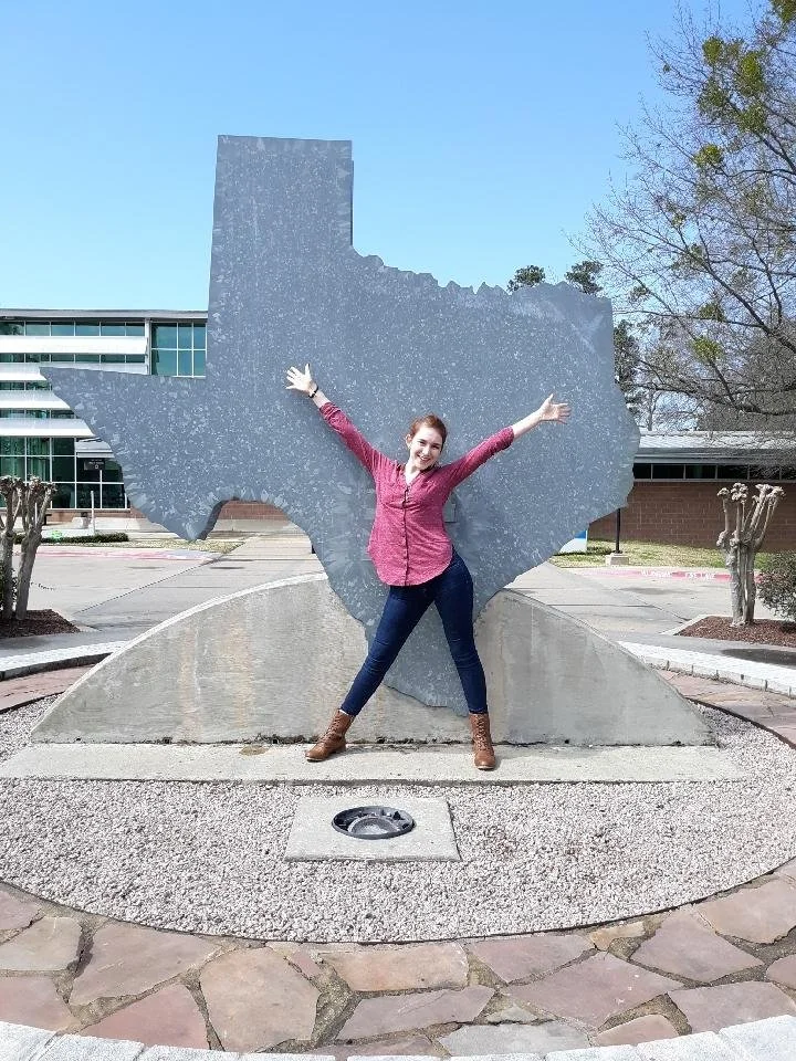 A woman wearing a pink shirt and standing in front of a large statue of Texas