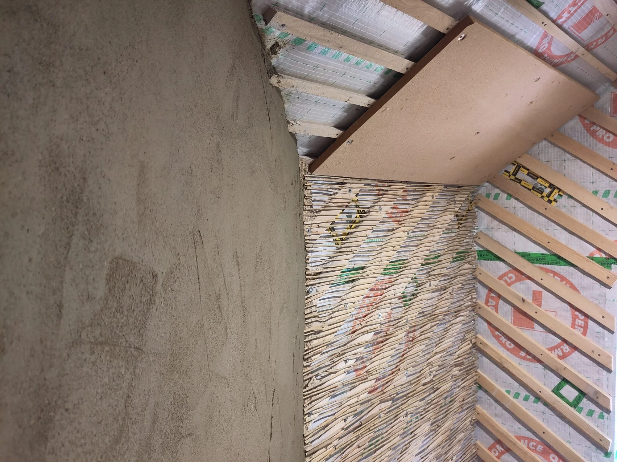 Santier cu pereti in diferite stadii de finalizare, cu membrana de vapori, sipci oblice, rogojina de stuf si tencuiala de argila