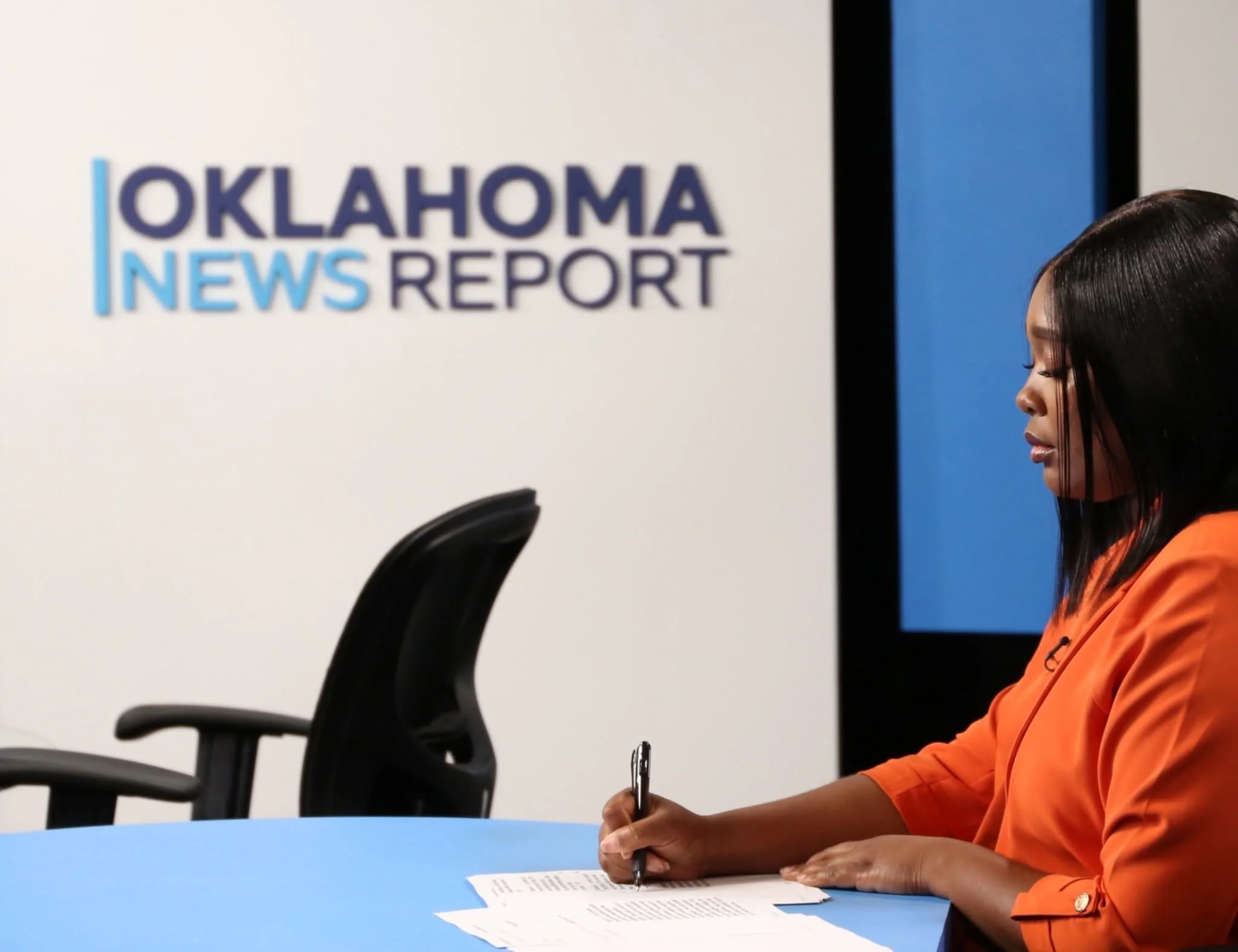 News anchor in a beige suit with a pink pocket square reports in a studio. Behind him on a large screen, is the Oklahoma City Thunder logo, a photo of celebrating basketball players, and the text "WORLD CHAMPIONS".