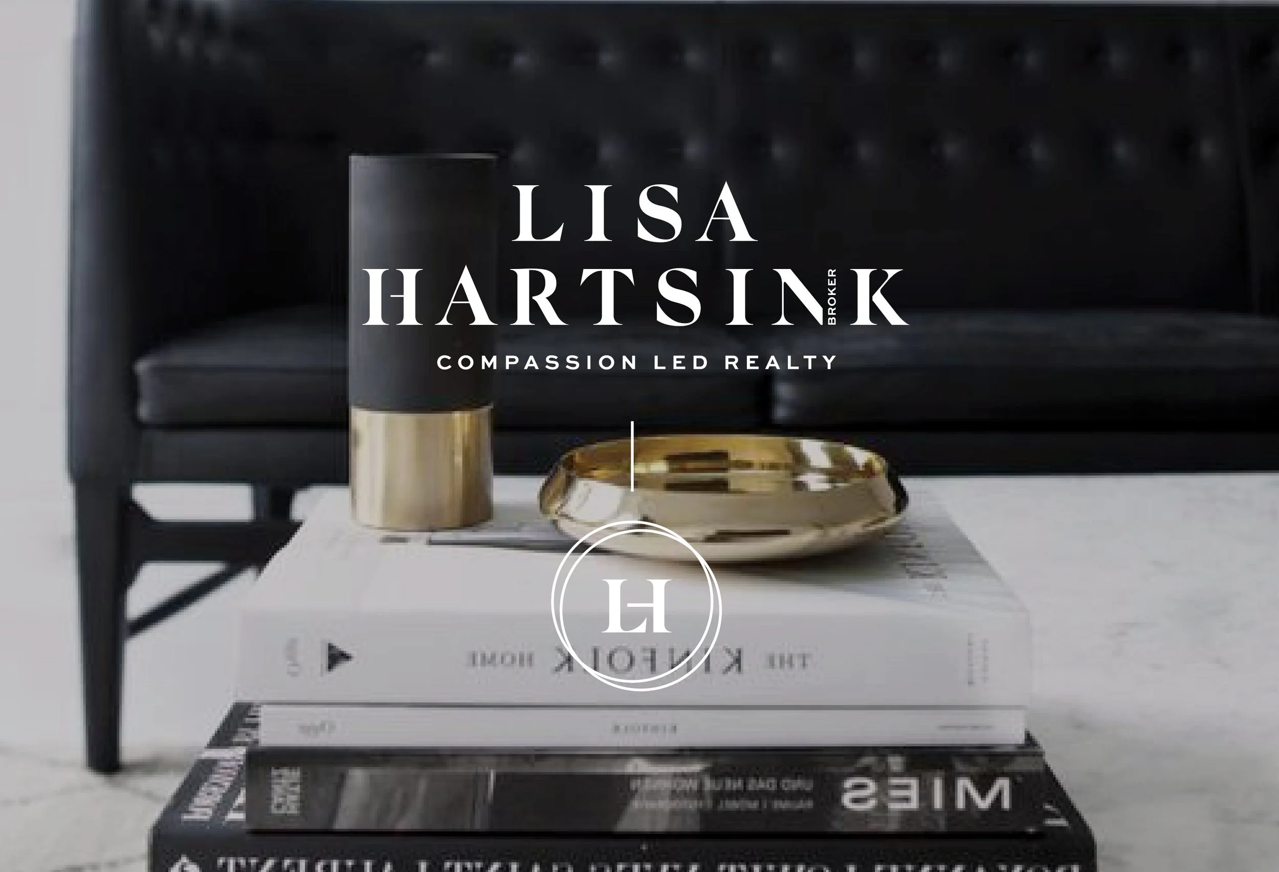 Close-up of a black box with white text overlay displaying marketing or branding information for Lisa Hartsink, a real estate broker. The box contains a gold and black candle, with a gold decorative object next to it, all placed on a white surface against a dark, tufted background.