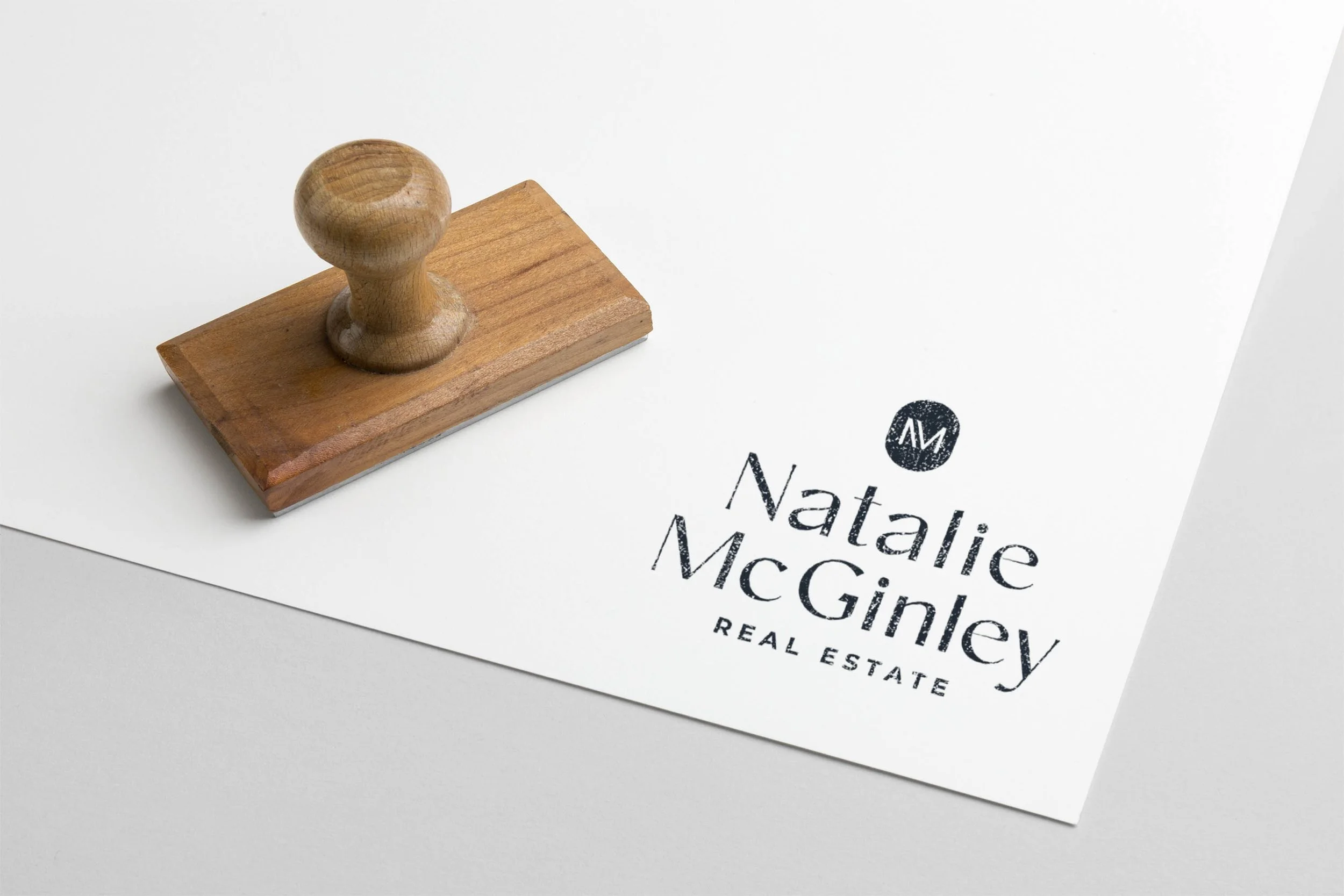 Wooden ink stamp next to a paper with stamped text "Natalie McGinley Real Estate."