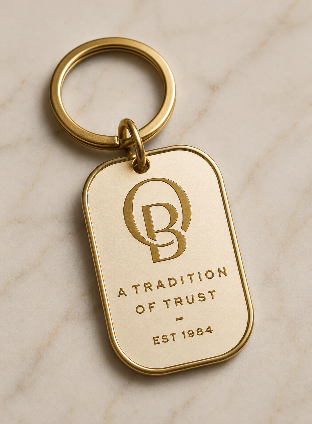 Gold keychain with engraved logo and text reading "A TRADITION OF TRUST - EST 1984" on a marble surface.