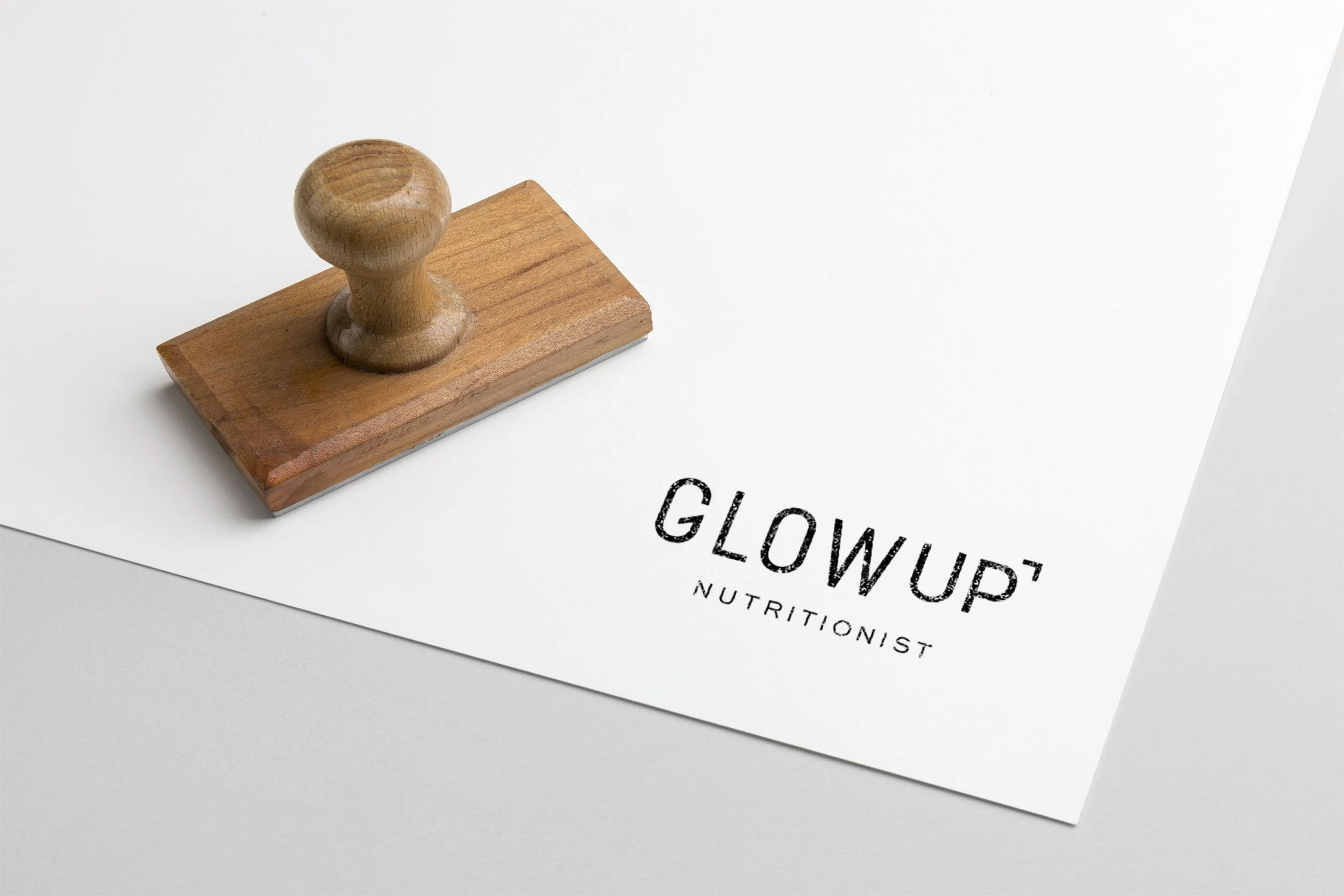 Wooden stamp with 'GLOWUP NUTRITIONIST' impression on white paper.