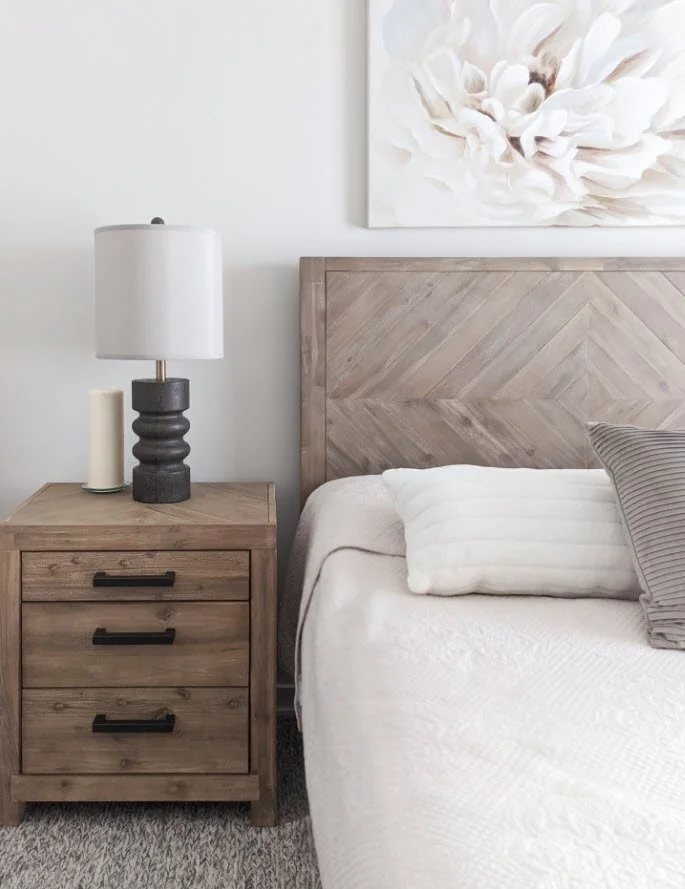 Bedroom with wooden nightstand, modern lamp, and bed with white and gray pillows.