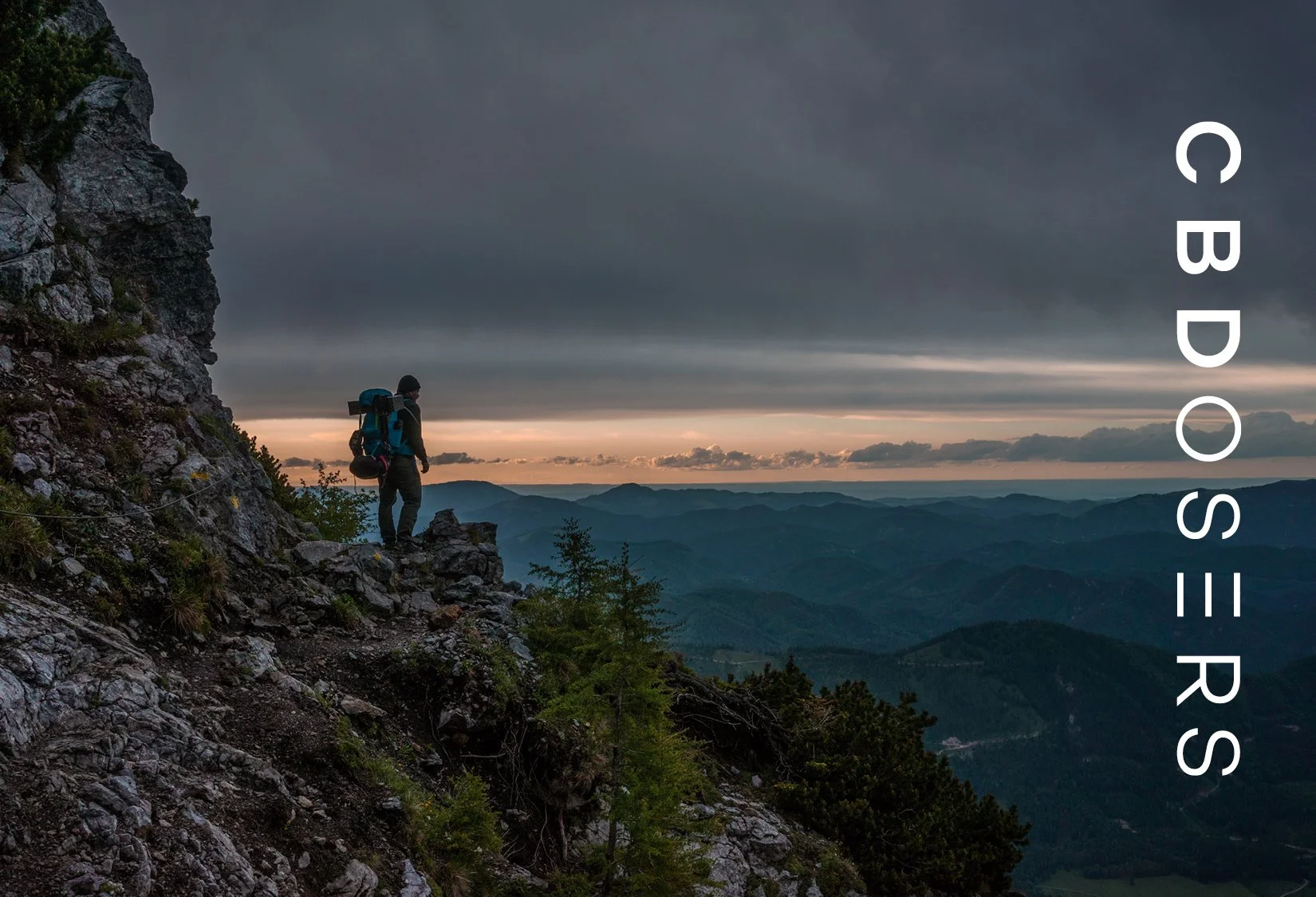 Hiker with backpack on mountain cliff at sunset, overlooking forested hills under a cloudy sky, with vertical text 'CBOSER' on the right.