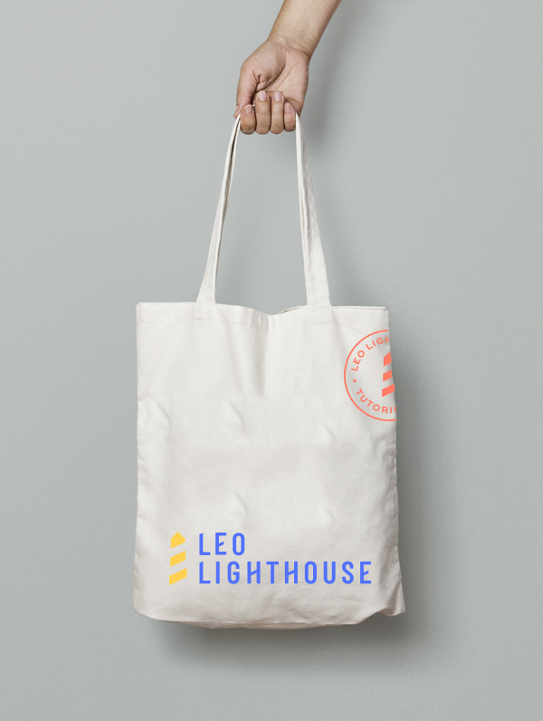A hand holding a white tote bag with the logo 'Leo Lighthouse' printed on it in blue and yellow, and a circular red logo on the upper right corner.