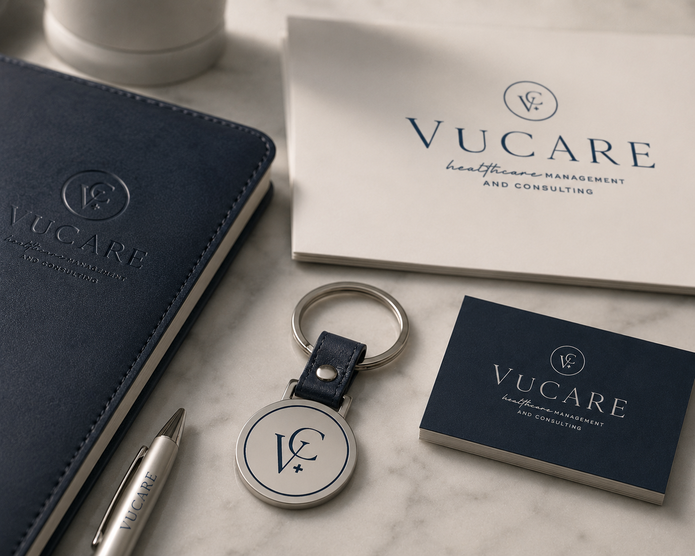Vucare branded notebook, pen, business cards, and keychain on a marble surface, with some white cups in the background.