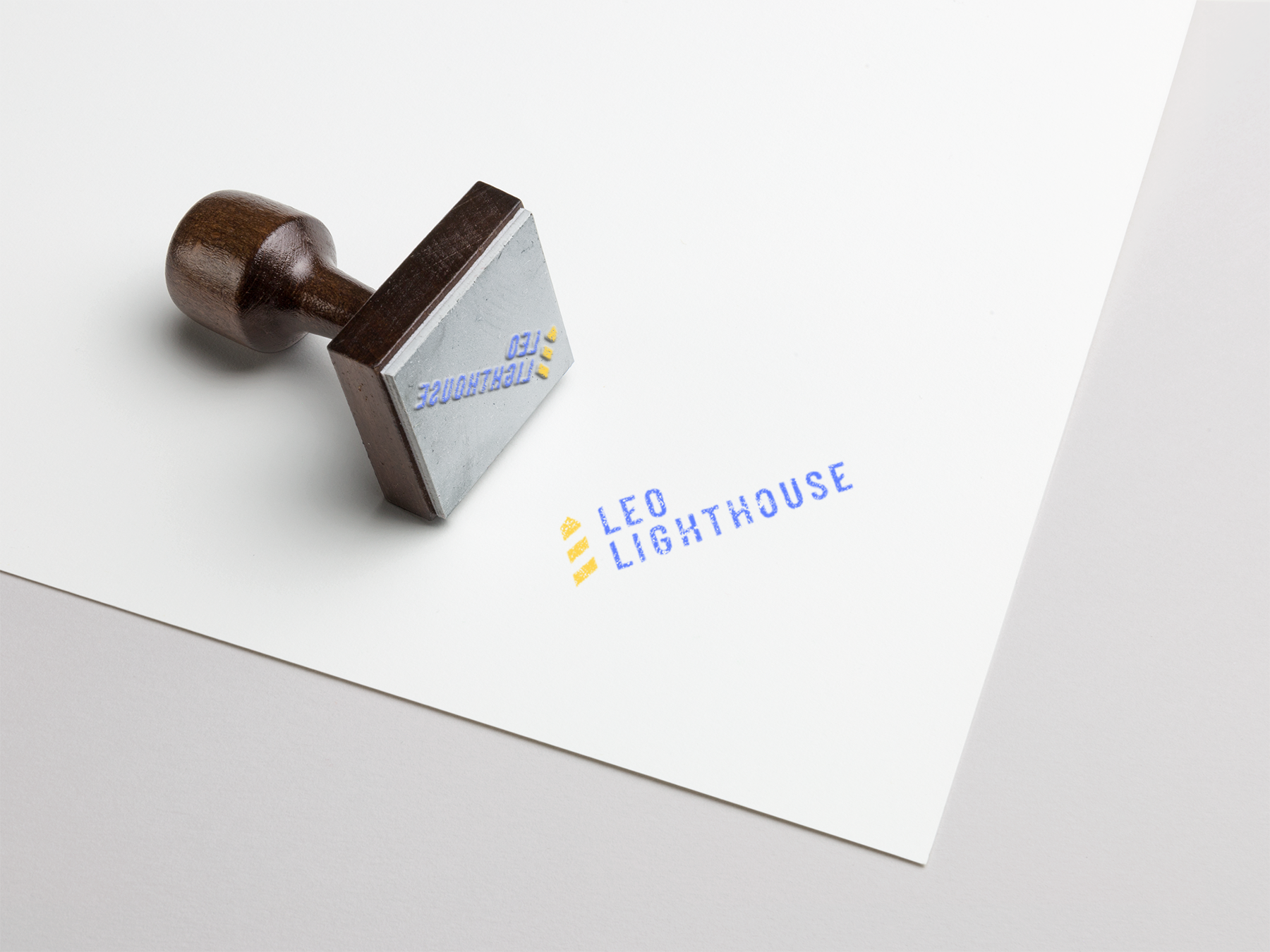 A rubber stamp with a wooden handle resting on a white sheet of paper that has blue and yellow text and markings, including the words "LEO LIGHTHOUSE."