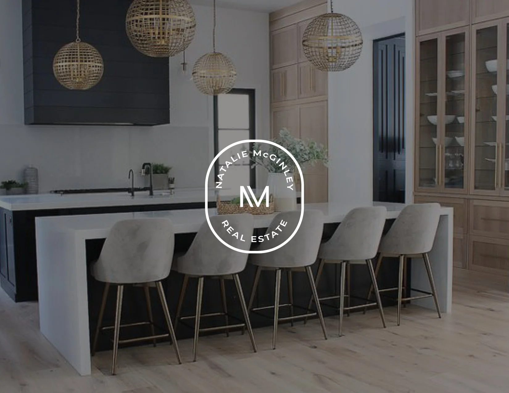 Modern kitchen with a white island, beige chairs, wooden cabinets, and decorative woven pendant lights.