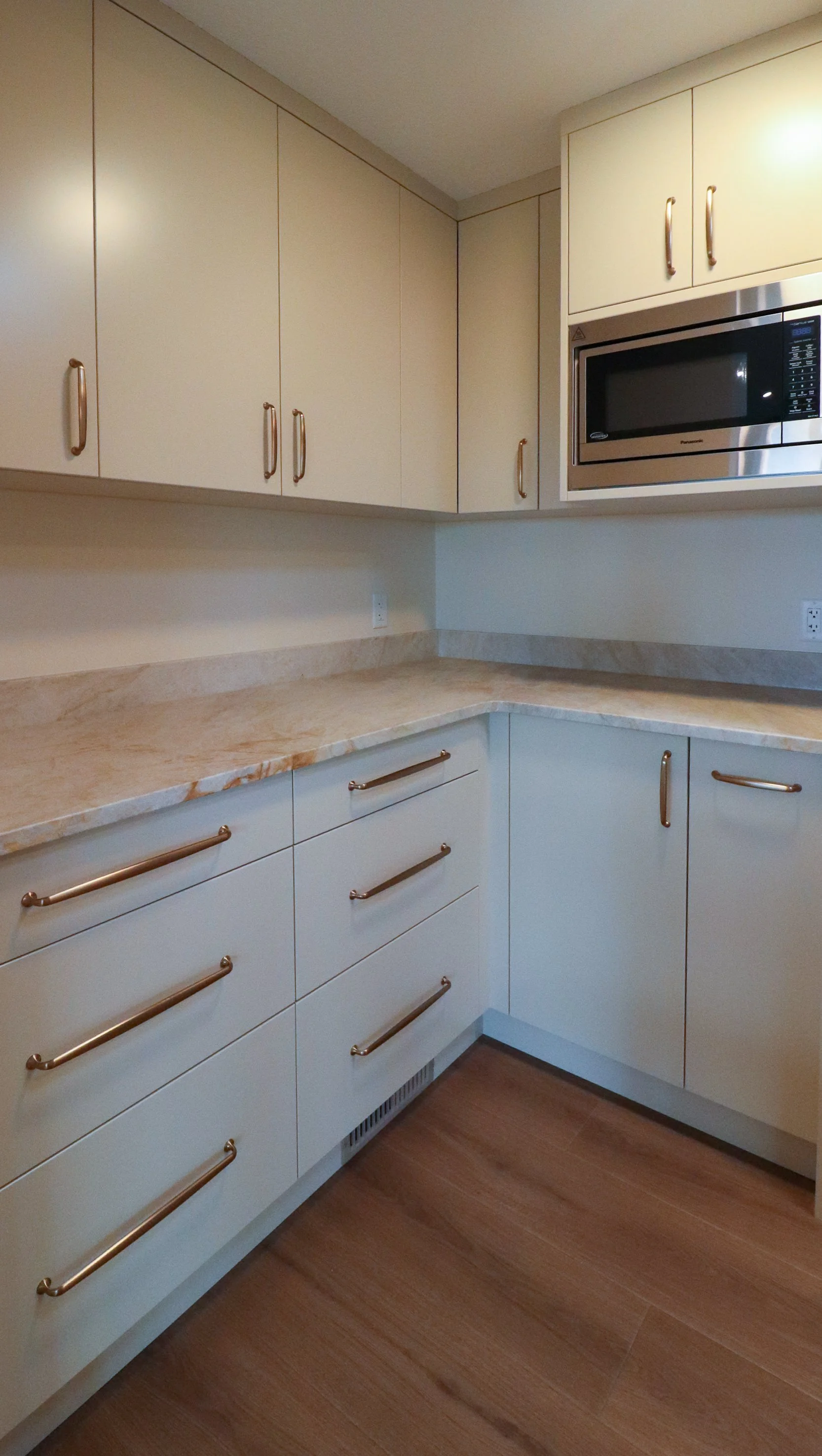 Utility kitchen with flat-panel cabinets, brass pulls and built-in microwave.