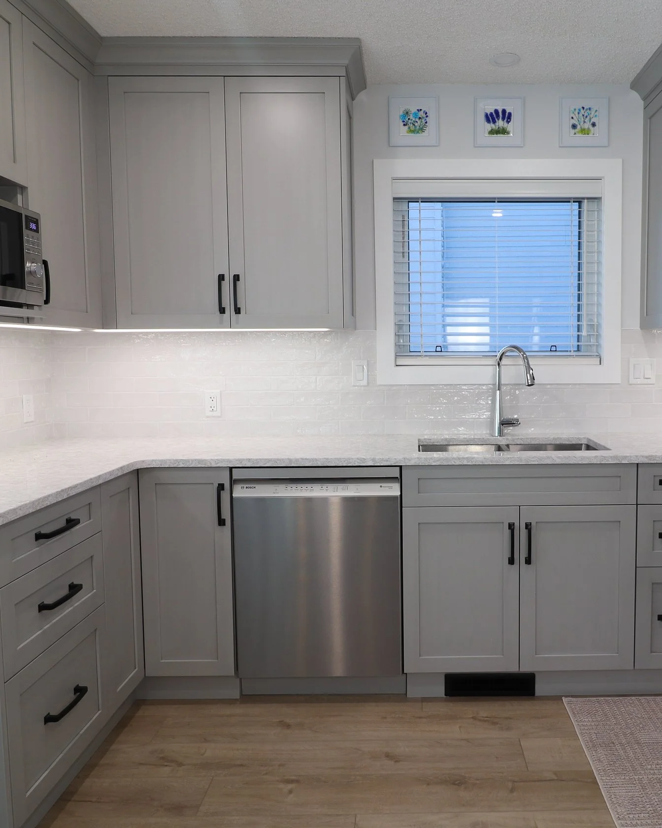 Sink beneath window with Stone Grey cabinets and stainless dishwasher.
