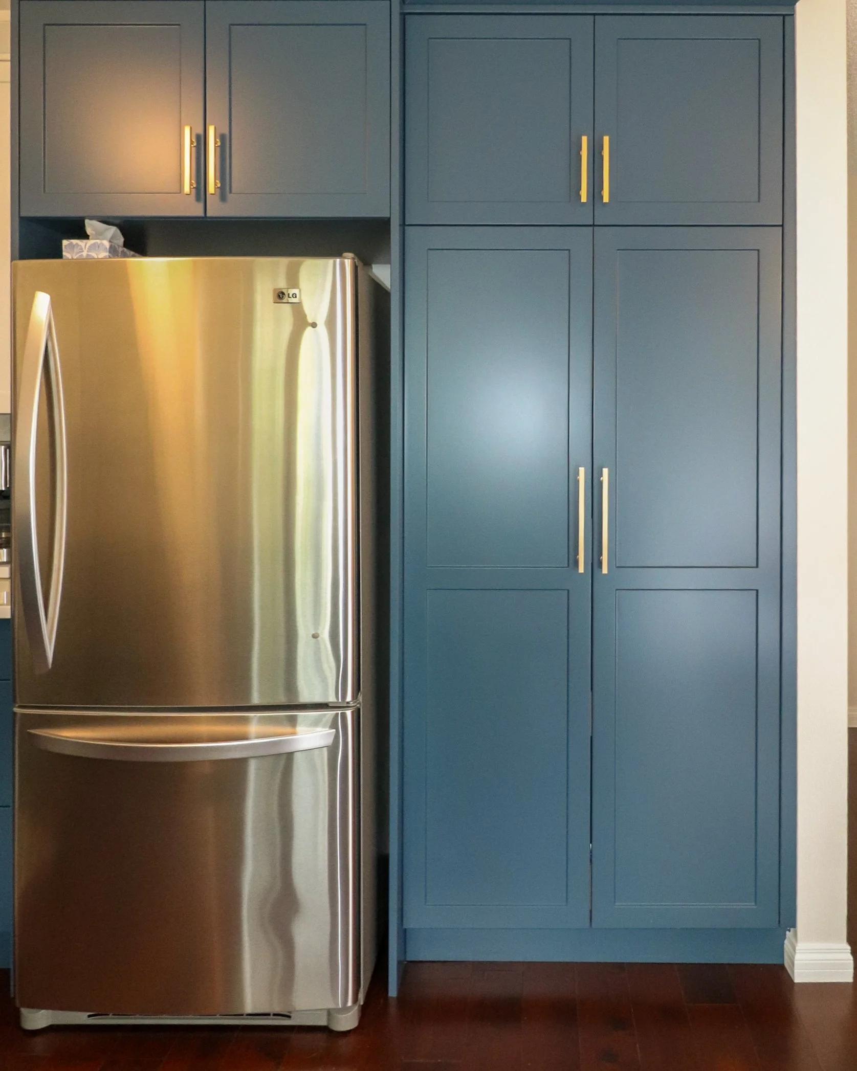 Refrigerator framed by floor-to-ceiling custom blue Shaker cabinetry.