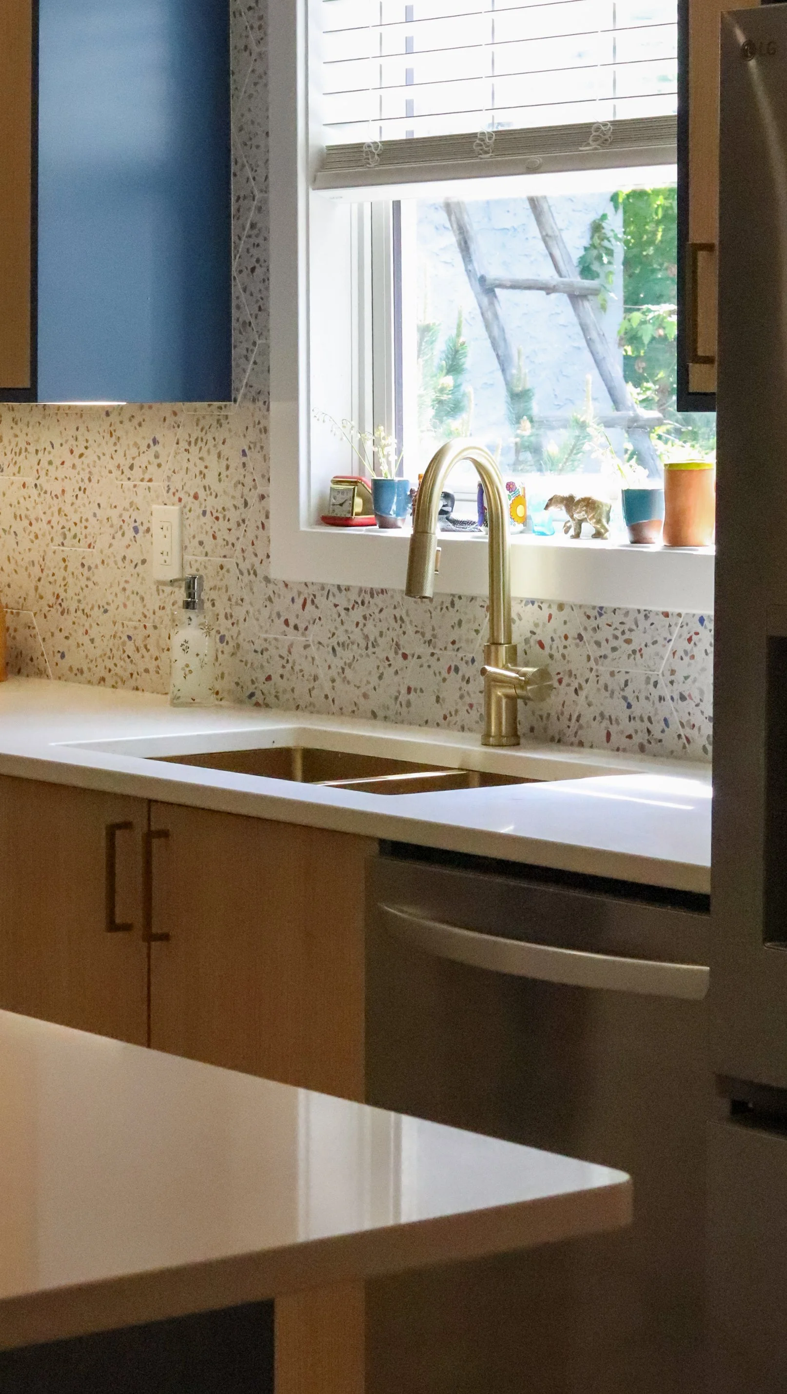 Window sink with champagne-bronze fixture, white countertop and hexagonal terrazzo backsplash.