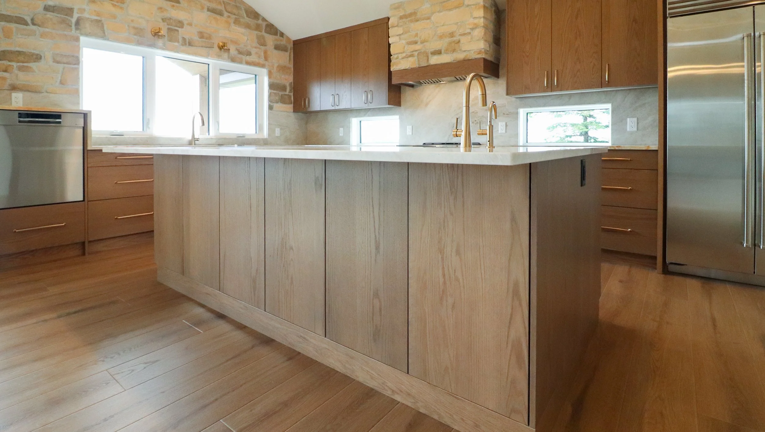 Oak kitchen island with prep sink, warm metal faucet and storage.