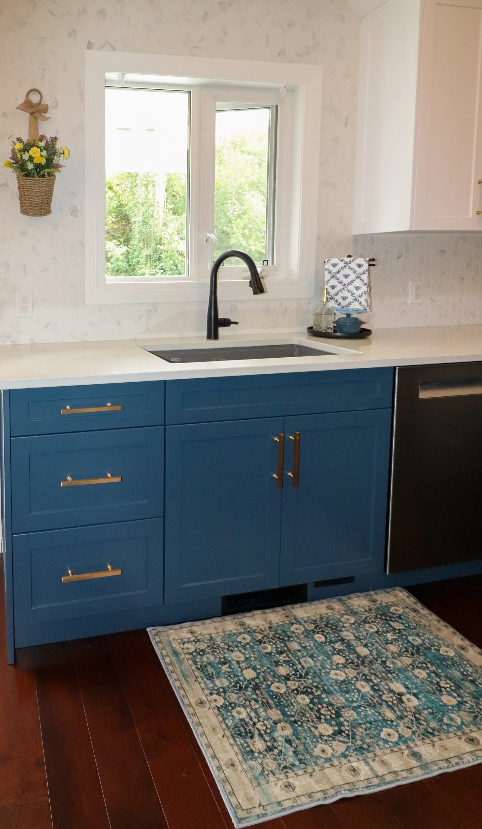Window-centred sink with blue cabinetry, dishwasher and matte black faucet.