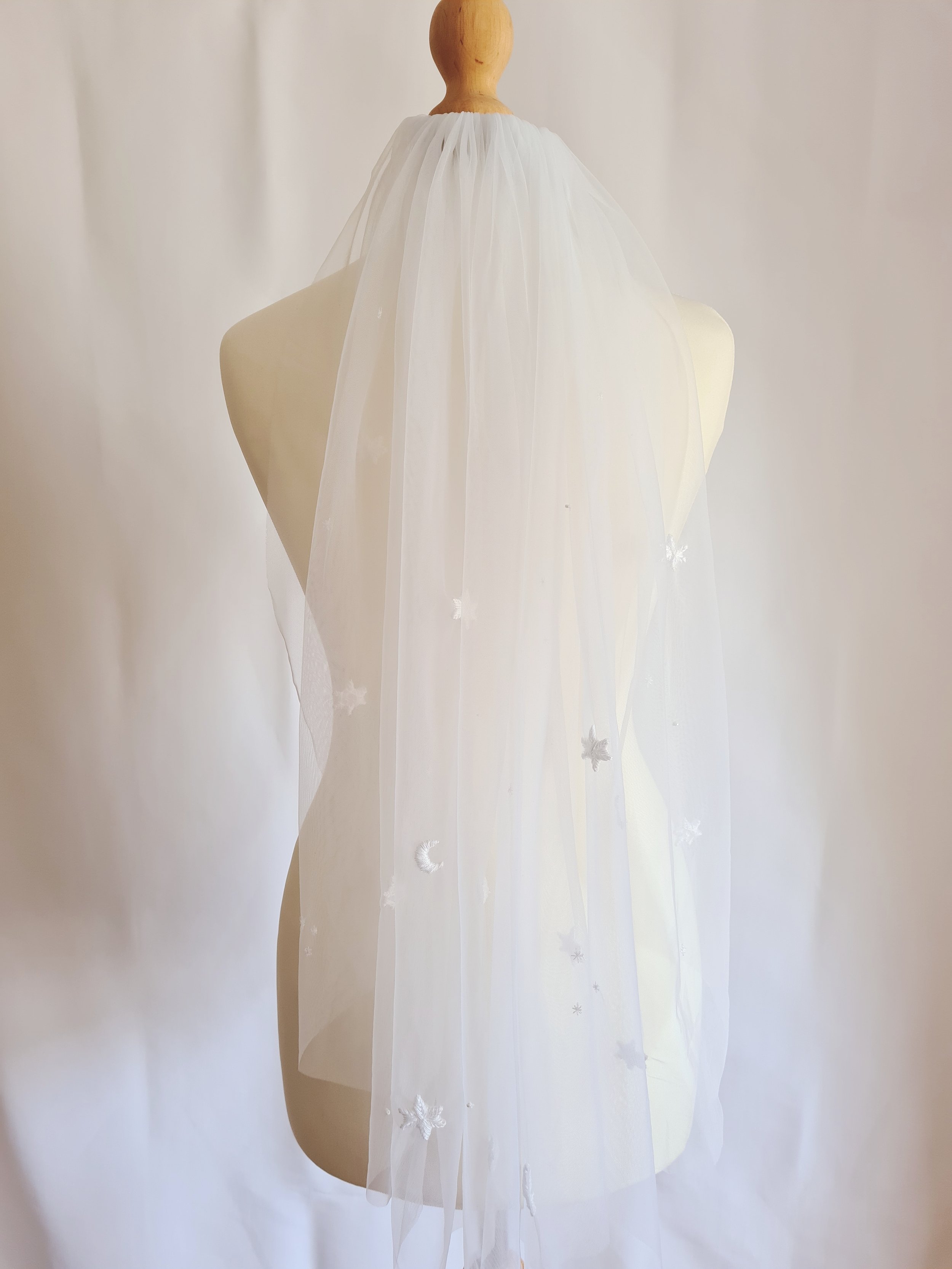 An ivory tulle celestial wedding veil with hand embroidered stars and moons on a mannequin