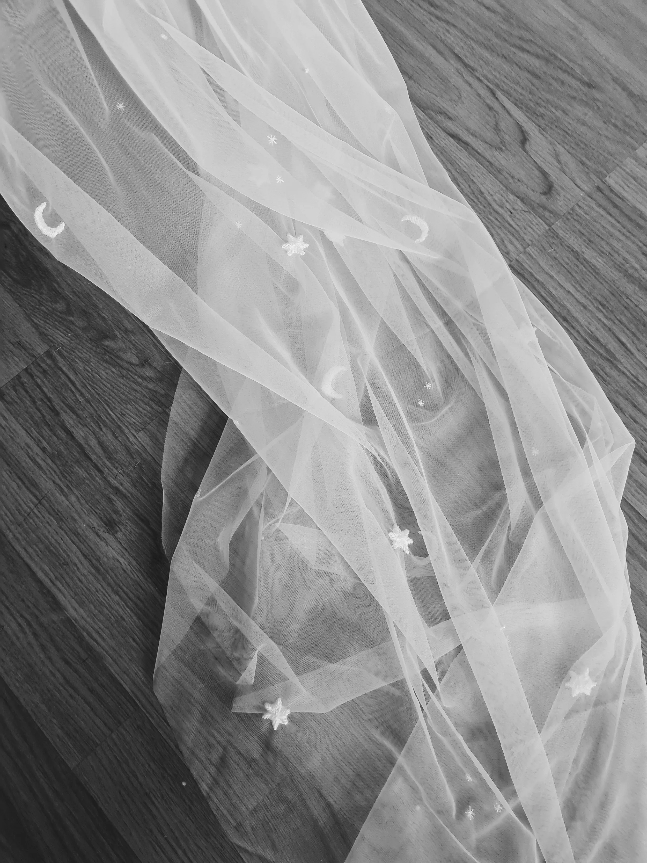 black and white photo of a celestial veil with embroidered stars and moons and tiny symbols in ivory