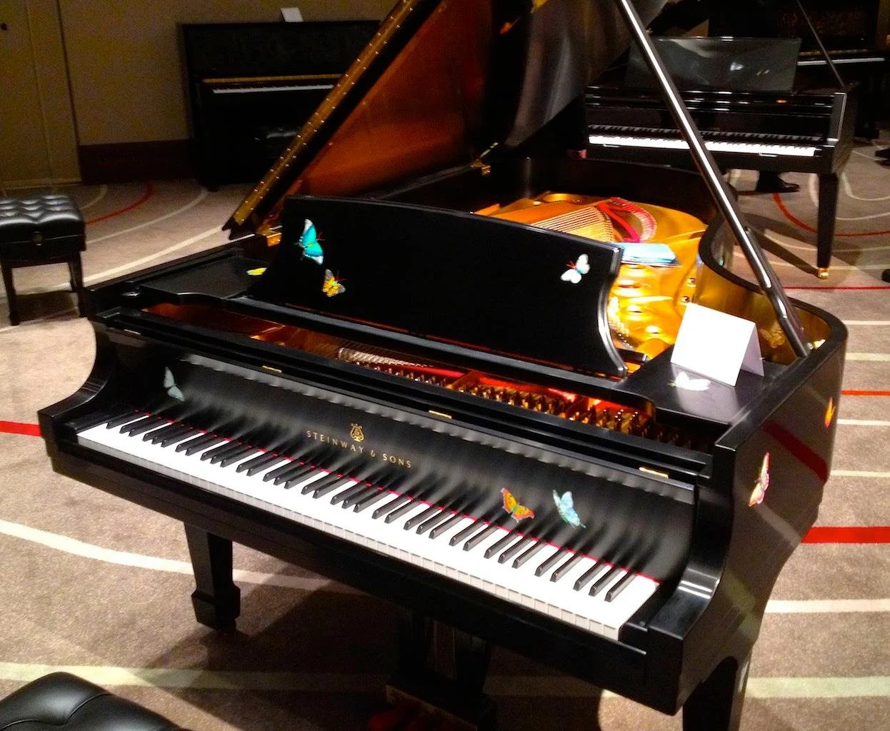 A black Steinway & Sons grand piano decorated with colorful butterfly stickers, situated in a room with a carpeted floor.