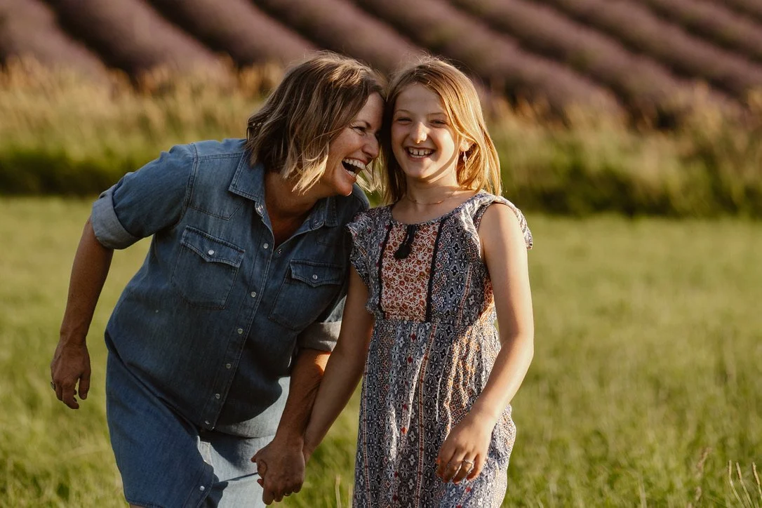 A woman and a girl are smiling and holding hands in a field, with lavender field in the background during sunset. Family photos, Hope ranch Lavender, Hood River