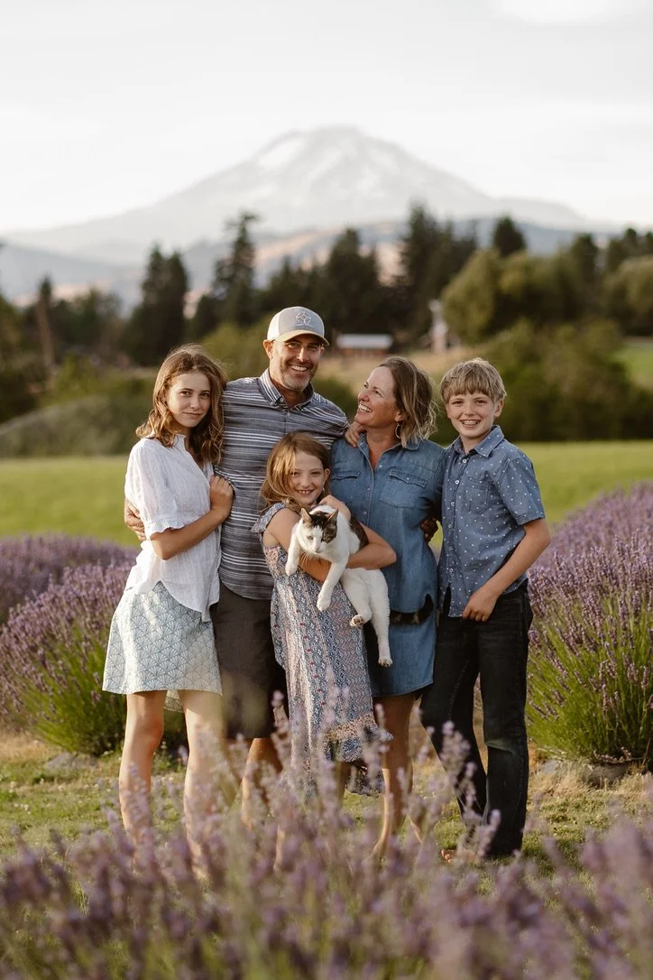 A family of five, including three children and an older woman, standing outdoors in a lavender field with Mount Adams in the background. They are smiling and holding a cat. Family photo, Photography Hood River, Venue, Hope Ranch Lavender