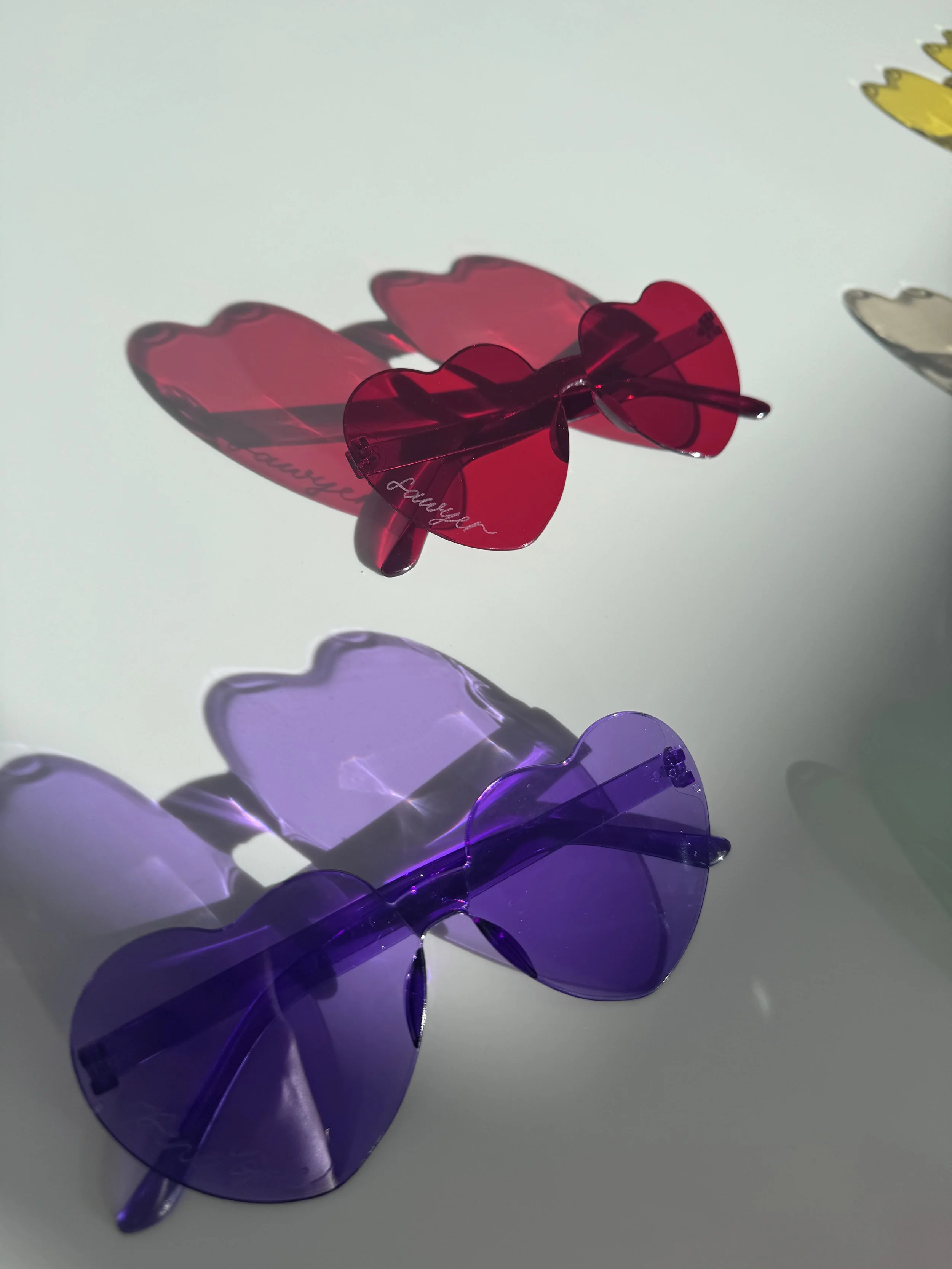 Decorative butterfly-shaped sunglasses in red and purple with shadows cast on a light-colored surface.