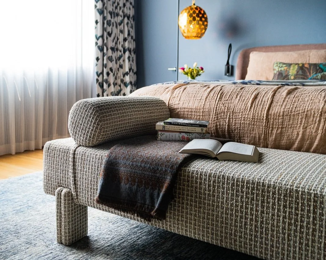 Custom upholstered bench at the foot of a bed in a bedroom designed by Violet Marsh Interiors, featuring tailored scale and textured fabric in a warm modern interior