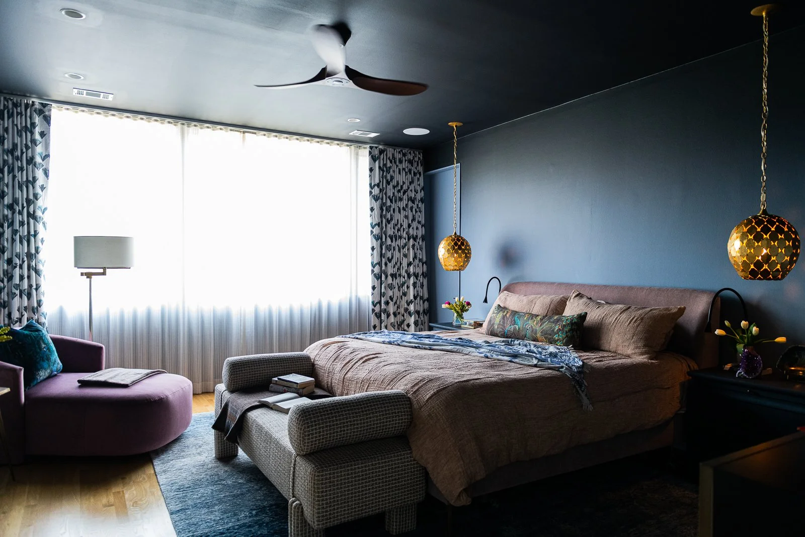 Moody jewel-tone primary bedroom in Virginia Highlands with ombré blue wallpaper, layered bedding, brass pendants, and custom upholstered bench
