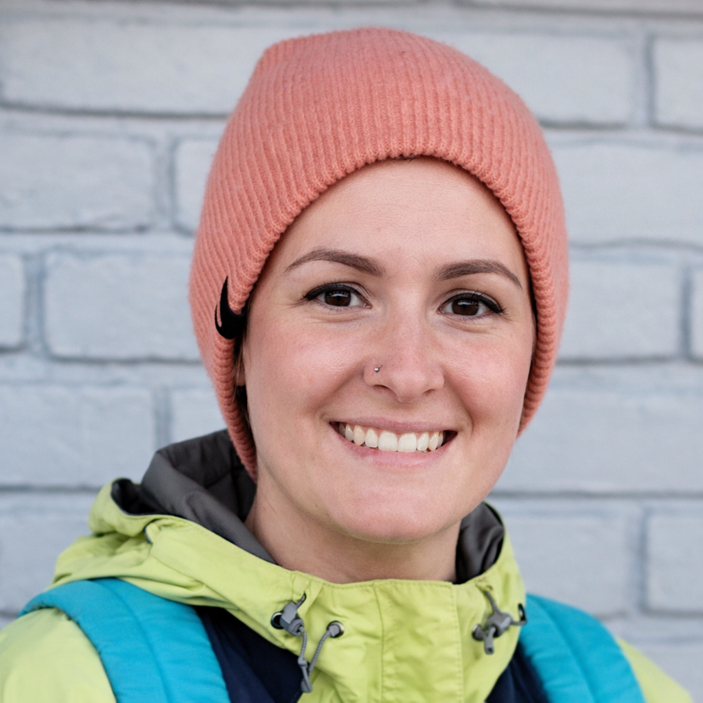 Woman in a peach beanie and lime jacket with turquoise backpack straps