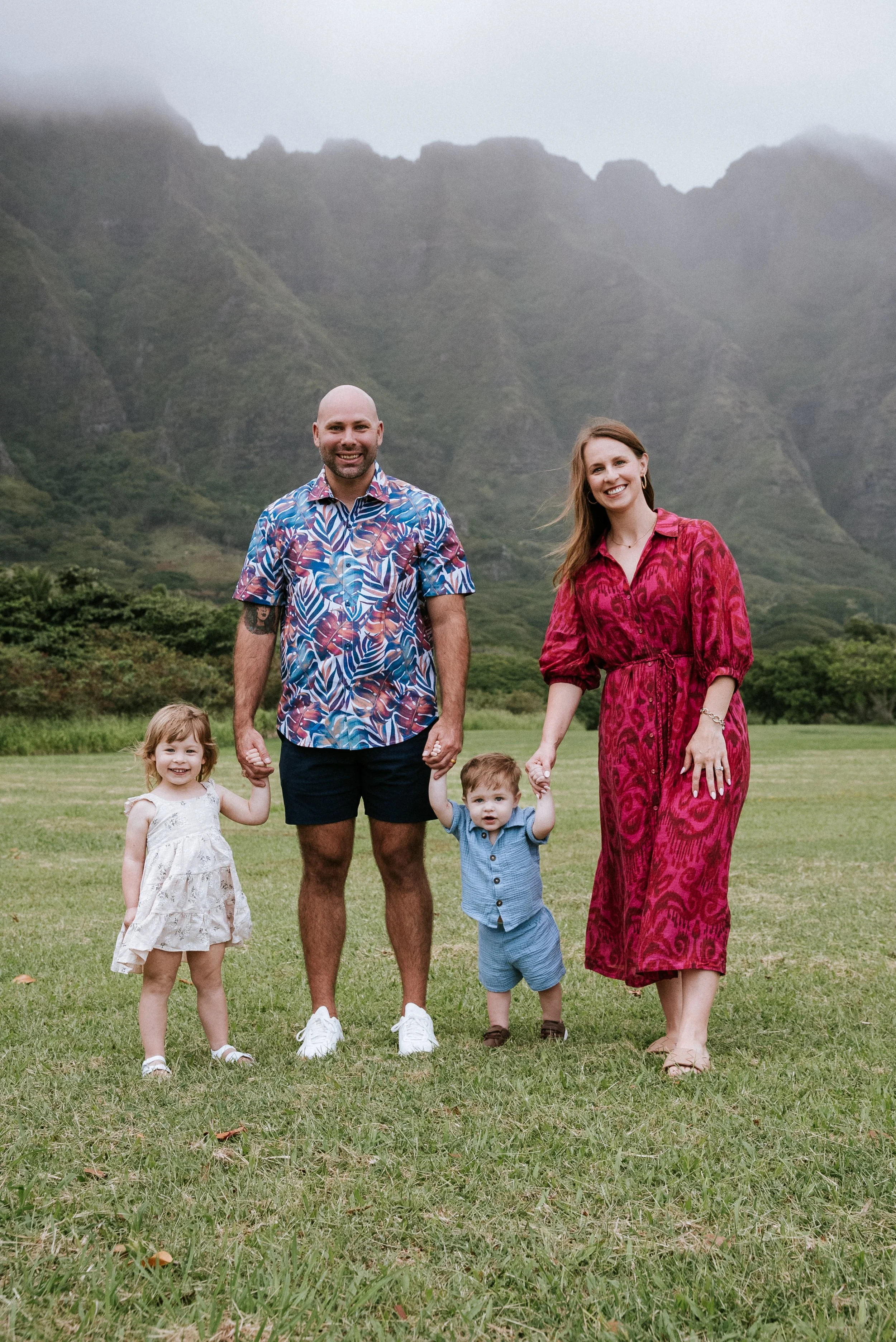Family of four standing on a grassy field with mountains in the background