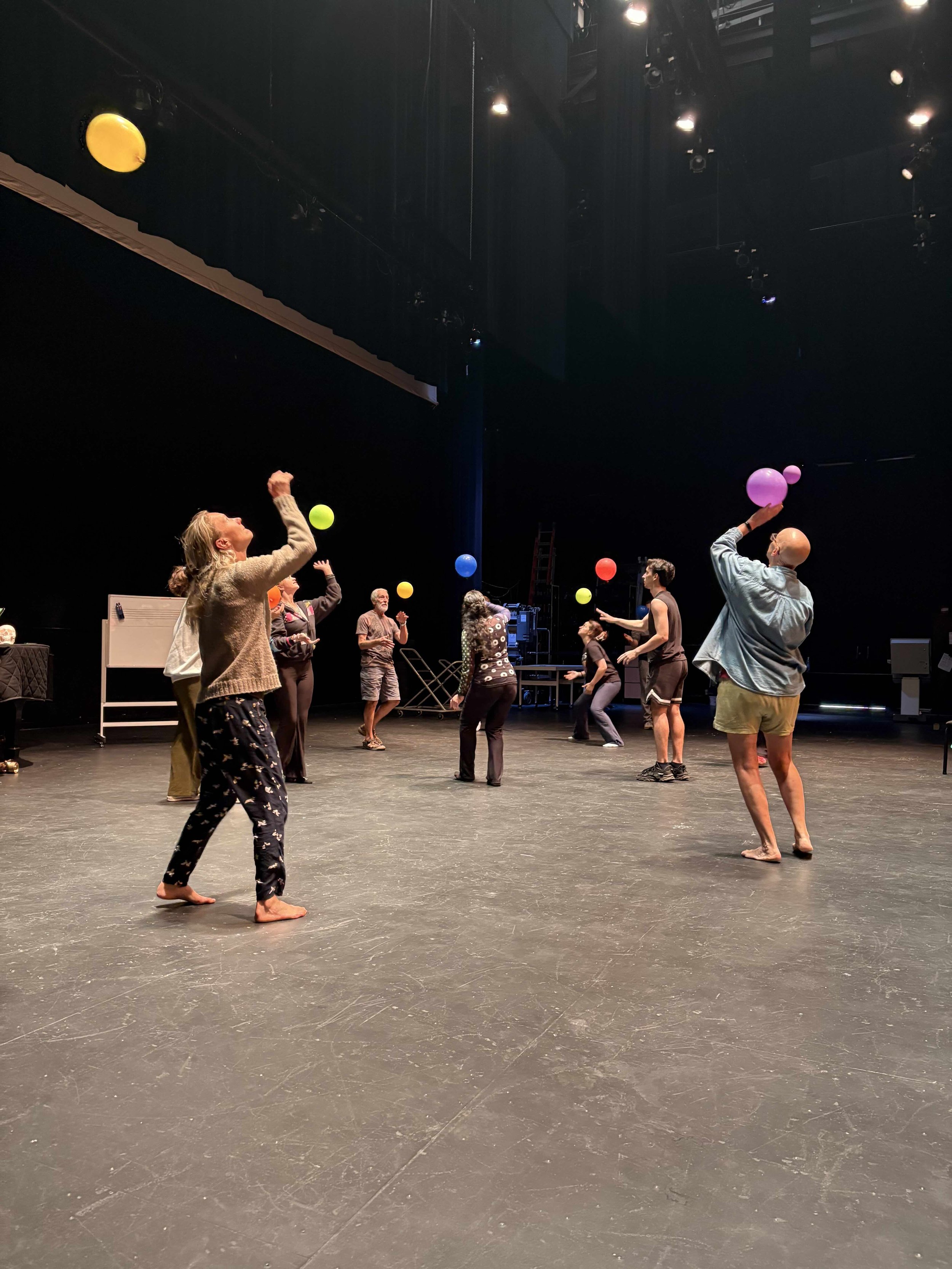 People playing with colorful balloons on stage in a theater or rehearsal space.