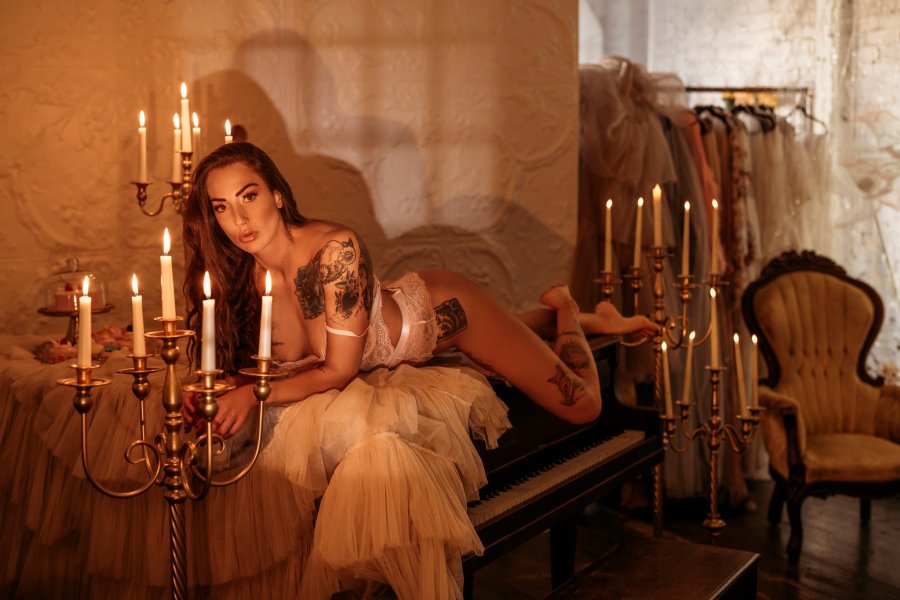 A woman with tattoos lying on a bed decorated with candles in a dimly lit room.