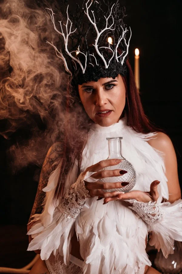 Fallen angel close-up: antler crown, swirling smoke and glass bottle, cinematic Halloween boudoir
