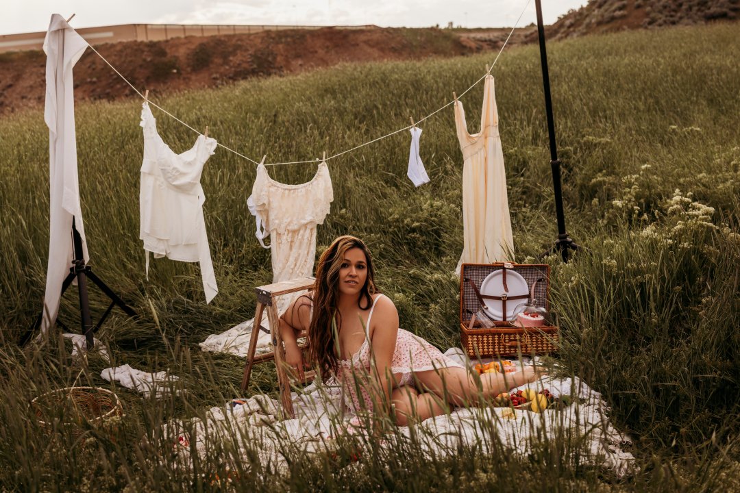 A woman lying on a blanket in a grassy field with a clothesline hanging laundry behind her and a picnic basket nearby.