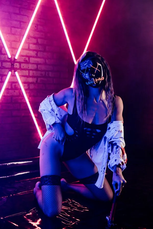 A woman lit by colored gel lighting in a dark, moody studio with drifting fog
