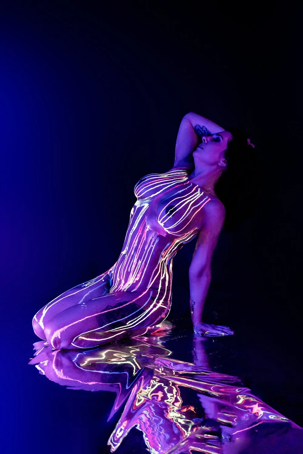 A figure kneeling, glowing with neon body paint under blacklight