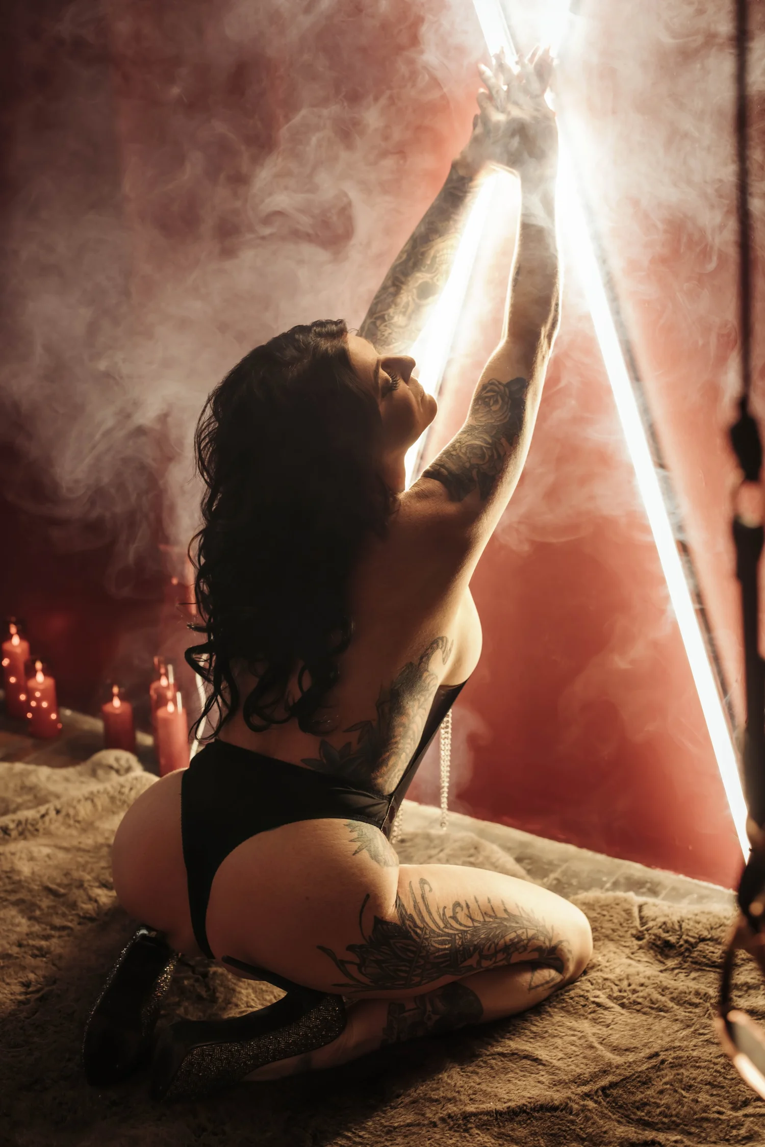 A woman kneeling with arms raised amid neon light and soft smoke