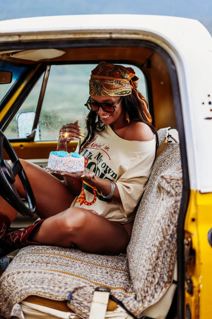 A woman celebrating her birthday with a cake and sparklers inside a vintage yellow vehicle.