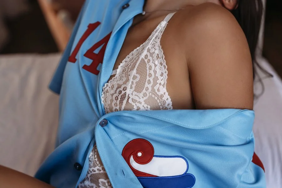 Close-up of a person's shoulder and upper chest, wearing a light blue jacket with red and white embroidery, partially open to reveal a white lace camisole underneath.