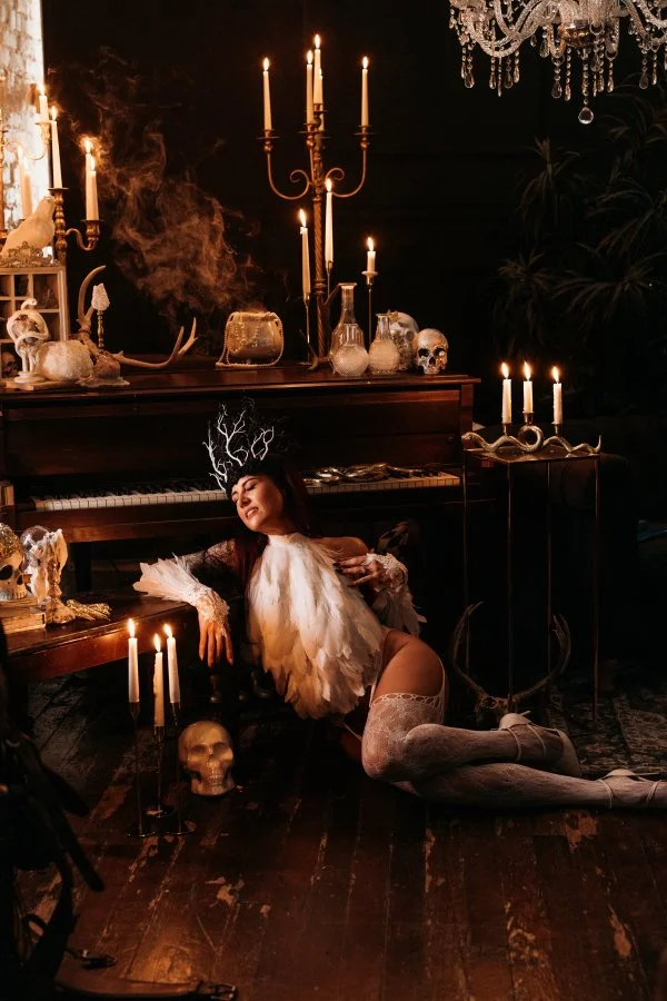 Fallen angel sprawled beside a grand piano in candlelight, skulls and chandelier, Salt Lake City boudoir