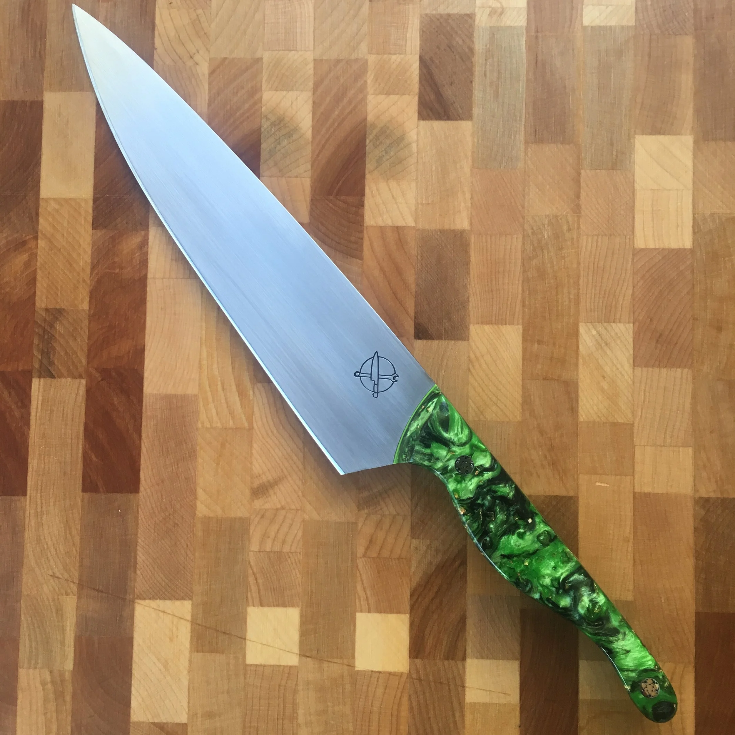 A large chef's knife with a green swirl handle, resting on a wooden cutting board.