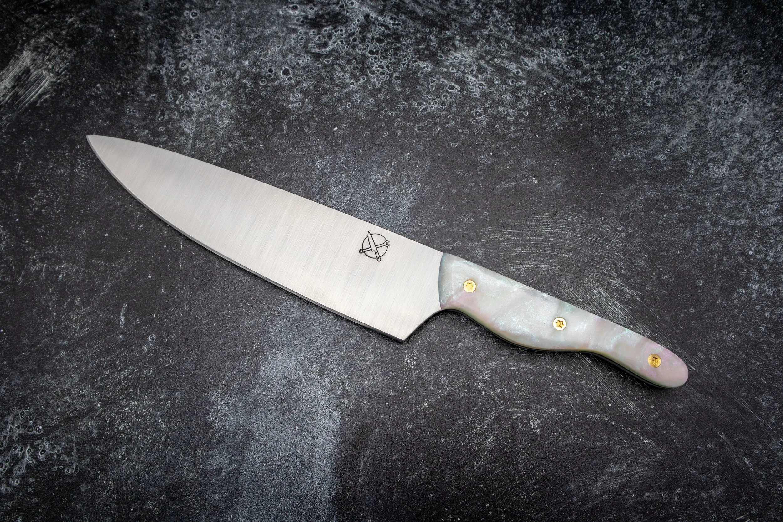 A stainless steel kitchen knife with a pearl-like handle and gold rivets on a black textured surface.