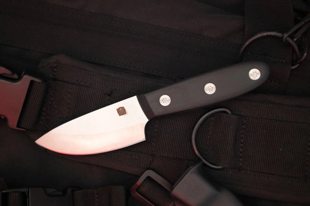 Blue Collar Blades S35V stainless steel Samson fixed blade knife with black G10 handle, resting on a black tactical backpack.
