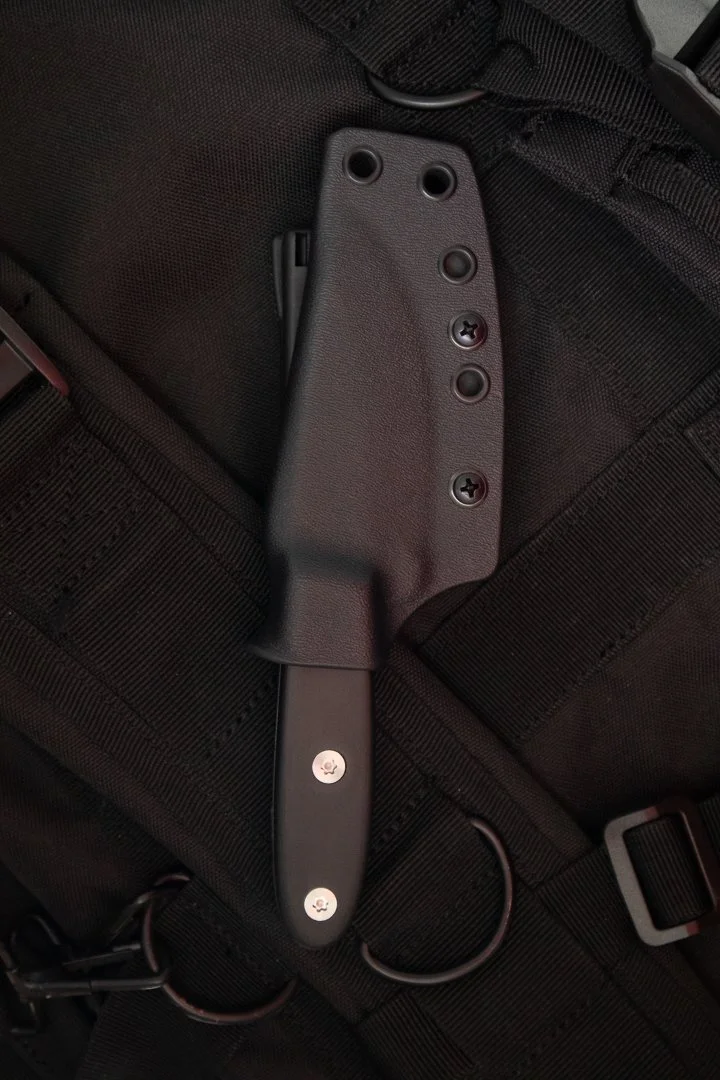 A black tactical knife with a handle mounted on a backpack strap.