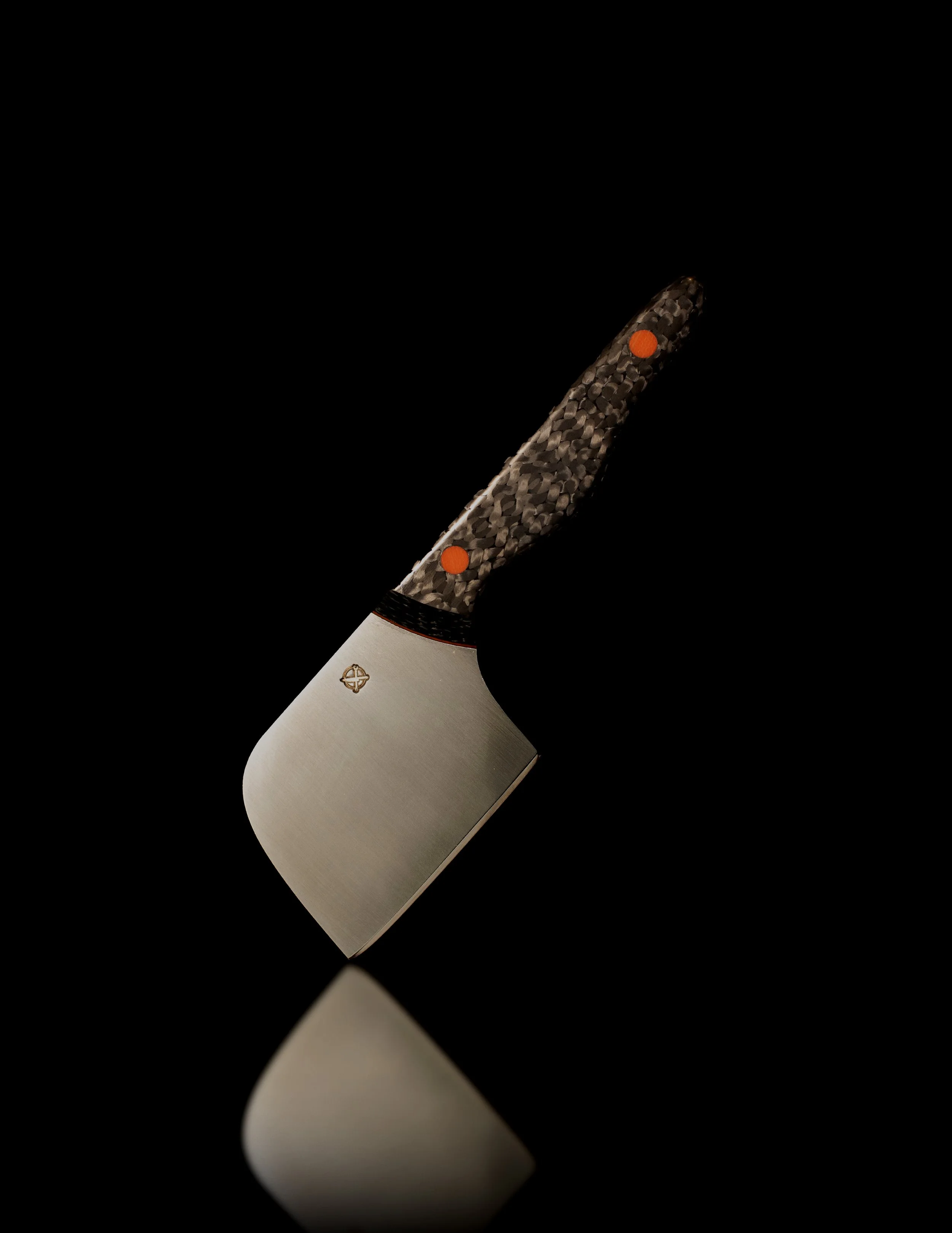 A sleek chopping axe with a textured black and grey handle, orange accents, and a shiny metal blade, reflected on a black surface.