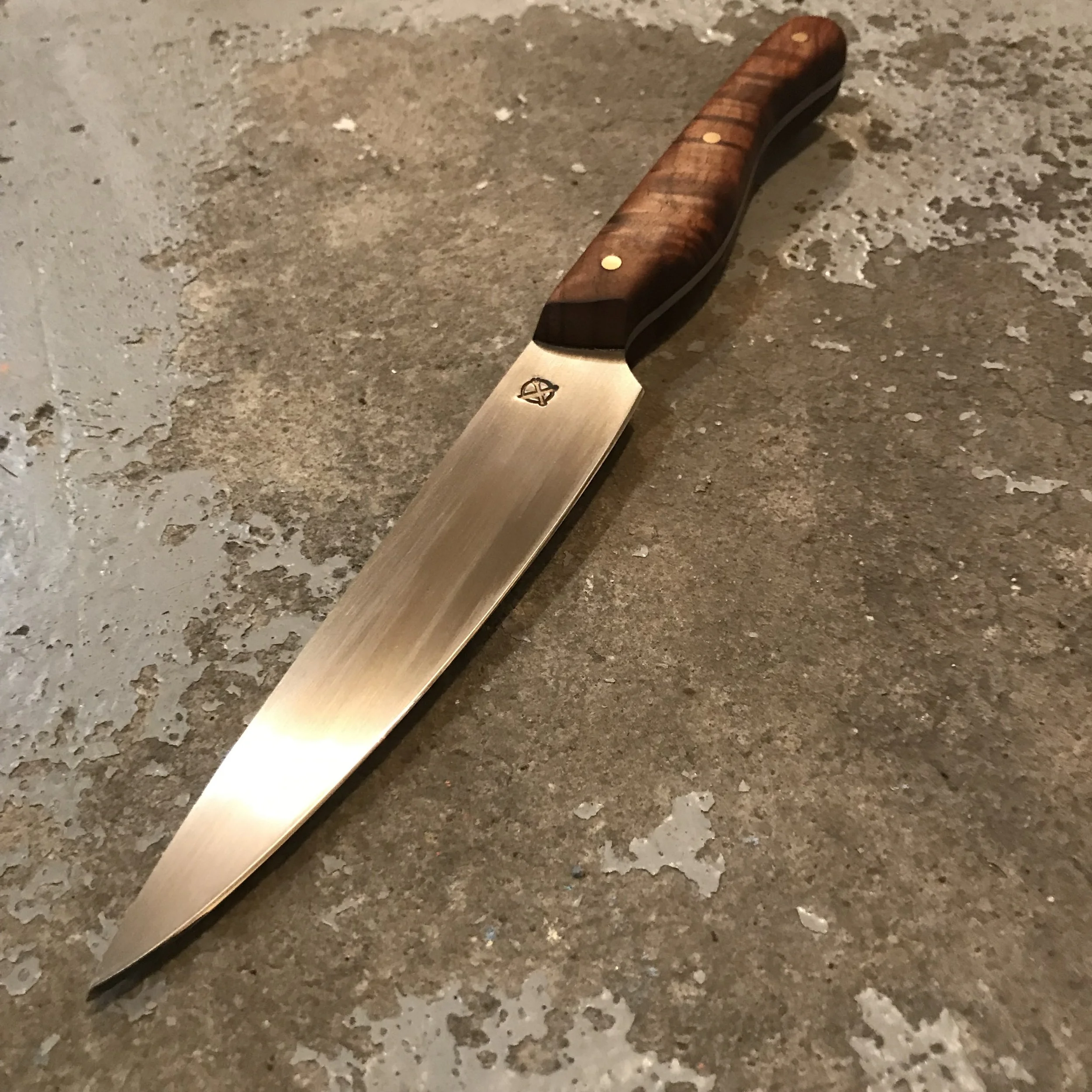 A kitchen knife with a wooden handle and a stainless steel blade lying on a textured, gray surface.