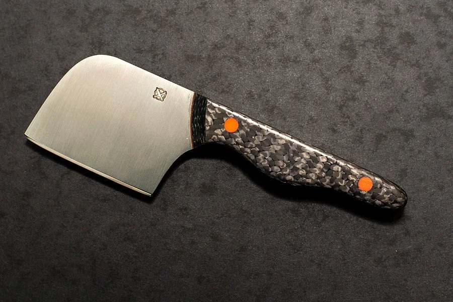 A cleaver with a broad, brushed metal blade and a textured black handle with orange accents, placed on a dark surface.