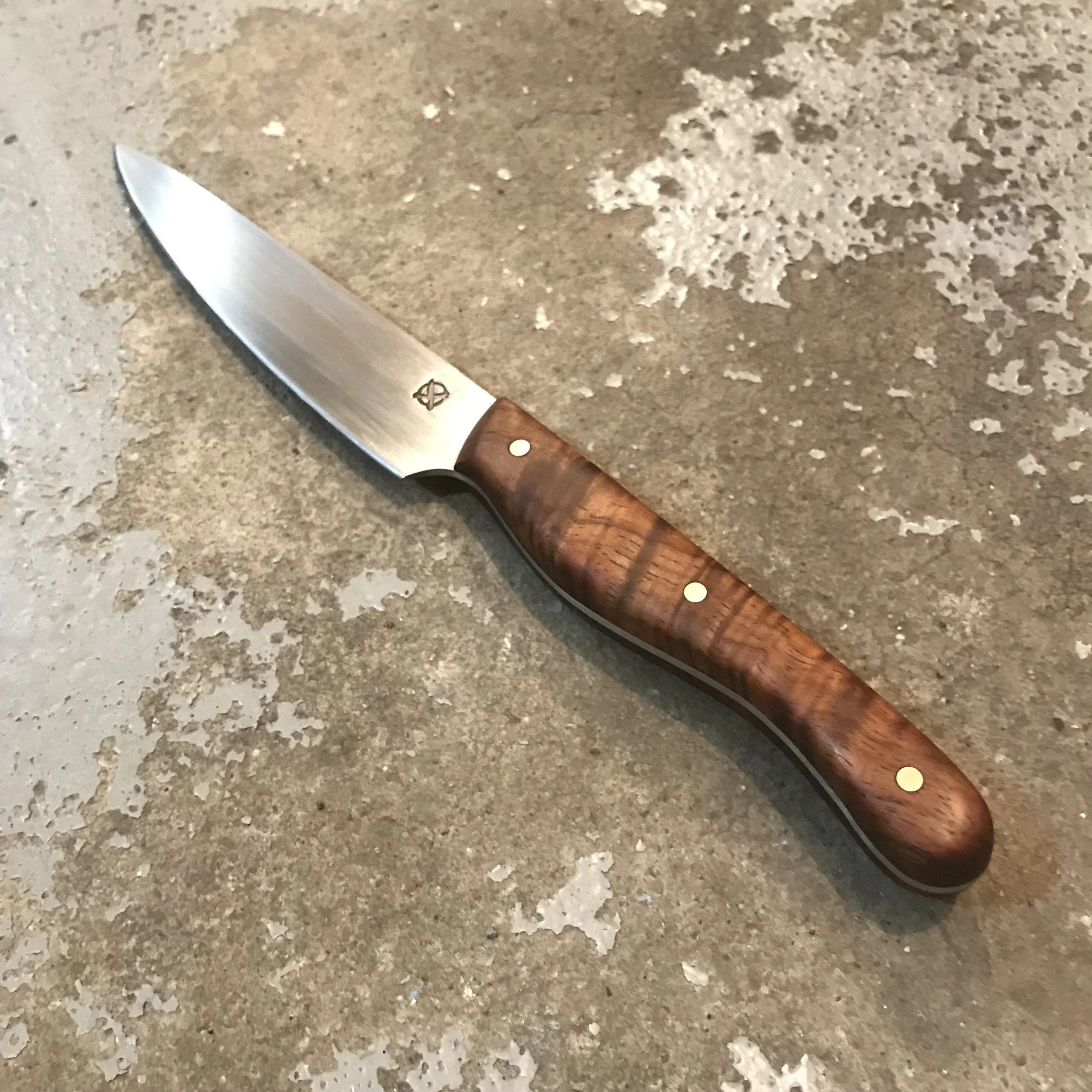 A kitchen knife with a stainless steel blade and a wooden handle resting on a textured, mottled gray surface.