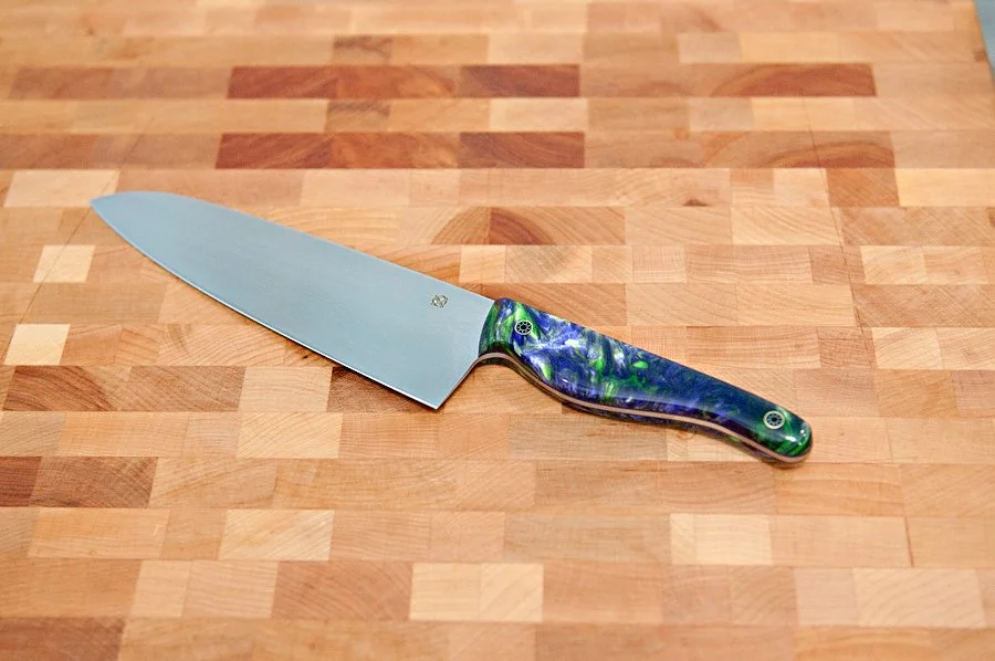 A kitchen chef's knife with a colorful, patterned handle resting on a wooden cutting board.